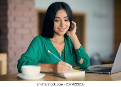 Unemployed Middle Eastern Young Woman Looking For Job Online, Sitting In Front Of Laptop And Taking Notes While Drinking Coffee, Checking Job Opportunities On Internet, Cafe Interior, Copy Space