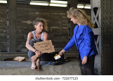 A Unemployed Punk Woman Sitting Under A Bridge With A Bottle Of Alcohol In A Brown Paper Bag Nearby Holding A Sign And Being Startled Getting A Gift From A Businesswoman