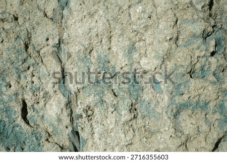 An uneven stone surface characterized by a unique pale green and teal patina. The texture is porous and crumbly.