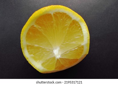             Unevenly Cut Half Of A Lemon With Juicy Pulp On A Black And Gray Background.                   