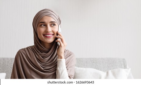 Unexpected Call. Young Arabic Girl In Headscarf Having Pleasant Phone Conversation At Home, Smiling And Looking Away, Panorama With Free Space