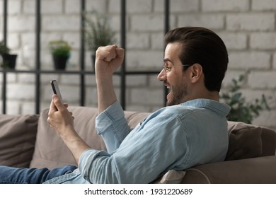 Unexpected Reward. Happy Overjoyed Millennial Man In Glasses Rest On Couch Looking At Cell Screen Scream Shout Yes In Euphoria Becoming App Game Winner. Shocked Excited Funny Guy Win Great Money Prize