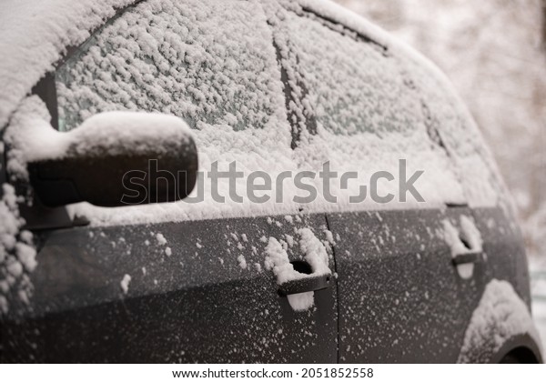 Unexpected snow\
covered cars and roads. Door mirror and glass of a car in the snow.\
Road safety. Selective\
focus