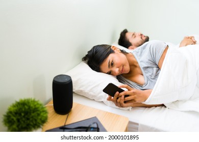 Unfaithful Young Woman In A Relationship Texting With Her Lover And Cheating On Her Boyfriend. Girlfriend Looking At Her Smartphone While Her Partner Sleeps