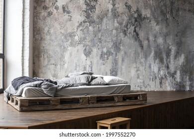 Unfilled bed made of wooden blocks with beige bedding in the bedroom against a wall with Venetian stucco. Scandinavian style