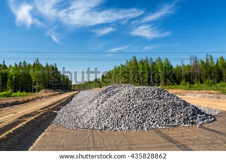 Unfinished asphalt country road in the forest. Pile of break stones on construction site