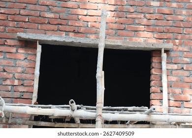 Unfinished brickwork shows a rectangular opening framed by bamboo scaffolding against an interior. Construction shows red bricks, gray mortar, bamboo, and dark void.