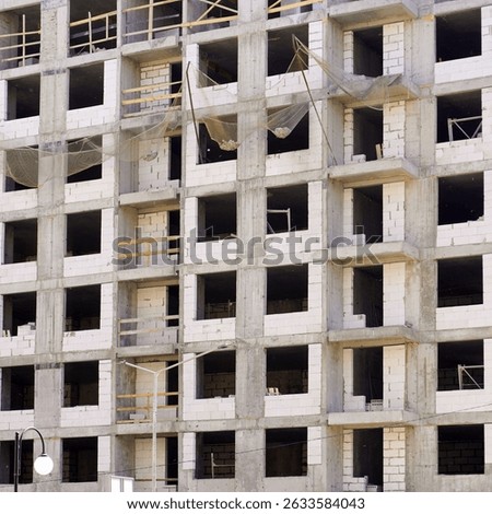 Unfinished building showing concrete frame, scaffolding, and safety net during construction