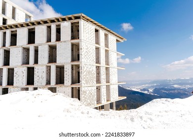 Unfinished house,building,hotel,mansion construction in winter snow forest in mountains,nature panorama.Ski alpine resort,travel.Calm countryside. Home residence in coniferous spruce pine trees