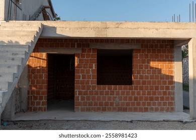 Unfinished residential building with red brick walls and concrete staircase under construction in sunlight. Concept of architecture, construction process, and structural development in urban areas.  - Powered by Shutterstock