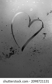 Unfocused inscription heart on frosty misted glass, a delicate thin contour of the heart as a symbol of romantic love, a symbol of sadness, loneliness. grayscale vertical frame with frost texture