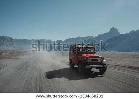Unfocused with motion blur shot of a red Off-Road Vehicle or Full-Sized SUV crossing the desert surrounded by mountains for commercial use