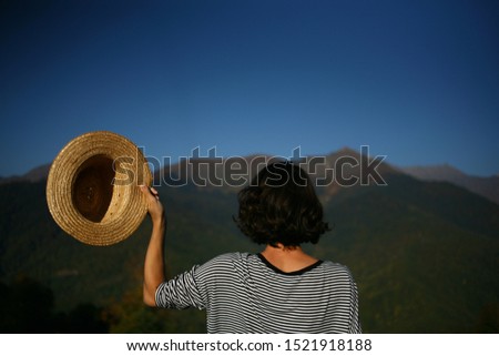 Unfocused natural background
with man traveler standing back on a mountain peak. Blurred girl in a straw hat overlooking the wildlife and sky. Tourism and outdoor activities.