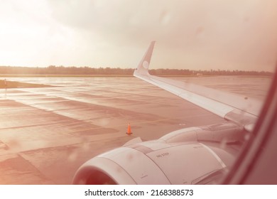Unfocused view of an airplane wing through a passenger window with raindrops
