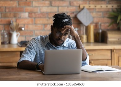 Unhappy 20s biracial man sit at home kitchen look at laptop screen frustrated by gadget problems. Mad young African American male distressed by slow internet connection, spam or computer breakdown. - Powered by Shutterstock