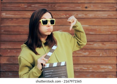 
Unhappy Actress Holding Film Slate Making Thumbs Down Gesture. Movie Critic Feeling Disappointed By Nest Motion Picture
