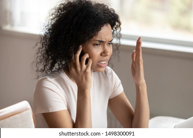 Unhappy african American millennial woman talk on smartphone upset hearing bad negative news, dissatisfied biracial female feel mad angry have unpleasant cellphone conversation or call