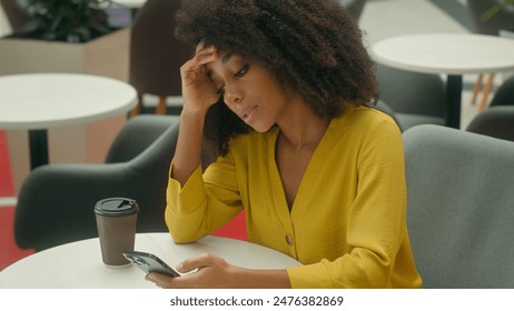 Unhappy African American woman in cafe holding head smartphone mobile phone cellphone notification sms message error loss upset female problem difficulties breakdown stressed sad girl tired trouble - Powered by Shutterstock