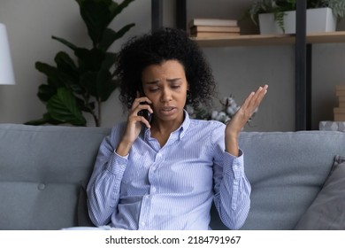 Unhappy African American Woman Talking On Phone At Home, Sitting On Couch, Dissatisfied Upset Young Female Having Unpleasant Conversation, Discussing Problems, Hearing Bad News, Complaining