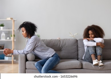 Unhappy african family annoyed angry single mother and upset teen daughter sit apart on sofa not talking after fight, stubborn teenager mom ignore each other, parent children misunderstanding concept