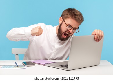 Unhappy aggressive man office worker screaming holding fist clenched, going to hit laptop display, bugs and errors in operating system, bad mood. Indoor studio shot isolated on blue background