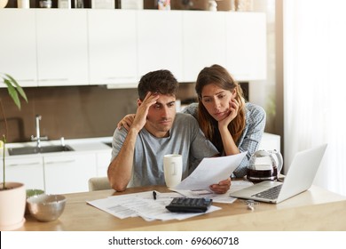 Unhappy American couple managing home accounts in kitchen, trying to save some money by cutting family expenses. Finances, bankruptcy, taxes, money, accounting and financial problems concept