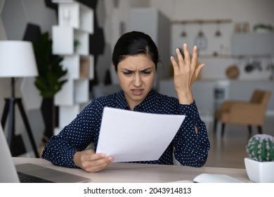 Unhappy annoyed Indian woman reading bad news in letter, sitting at home office desk, upset businesswoman or student holding letter, checking financial document, received unexpected debt notification - Shutterstock ID 2043914813