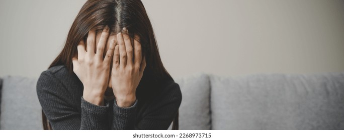 Unhappy anxiety young Asian woman covering her face with knee on the sofa in the living room at home. - Powered by Shutterstock