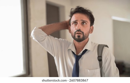 Unhappy anxious tired young adult boy wear formal dress standing in hallway. Sad Indian bearded man in tie touch hair thinking  deep thought about career lost jobless