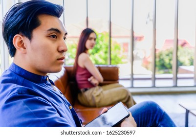 Unhappy asian couple by the man using internet in laptop and ignoring his girlfriend with sitting on couch in the living room. Couple in trouble concept. Photos focus at male.