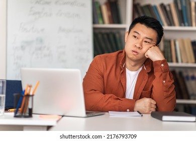 Unhappy Asian Male Teacher Sitting At Workplace Near Laptop And Whiteboard Having Problem With E-Teaching In Classroom Indoors. Modern Education Issue, Tutor's Professional Burnout Concept - Shutterstock ID 2176793709