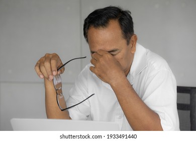 Unhappy Asian Older Man Taking Off Glasses From Tired Dry Irritated Eyes After Long Use. Elderly Male Worker Feels Blurry Vision Working On Laptop. Optical Overuse Of Aged Is Bad. (Selective Focus)