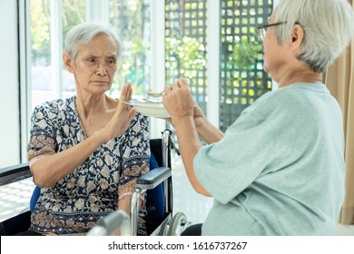 Unhappy Asian Senior Woman Rejecting,gesture Hand NO ,tired Old People Feeling Sick,dysphagia,dyspepsia Or Bored Of Food,friend Feeding Elderly Patient In Wheelchair,loss Of Appetite,anorexia Concept