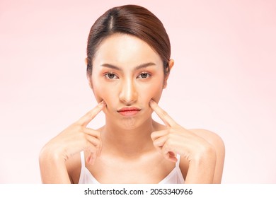 Unhappy Asian woman touching her cheek worry dry skin.Skin problem of beauty asian young woman having trouble of Dry skin, acne and wrinkles on pink background.Skin Problem Concept