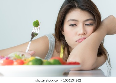 Unhappy Asian Women Is On Dieting Time Looking At Broccoli On The Fork. Girl Do Not Want To Eat Vegetables And Dislike Taste Of Broccoli.