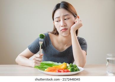 Unhappy Asian Women Is On Dieting Time Looking At Broccoli On The Fork. Girl Do Not Want To Eat Vegetables And Dislike Taste