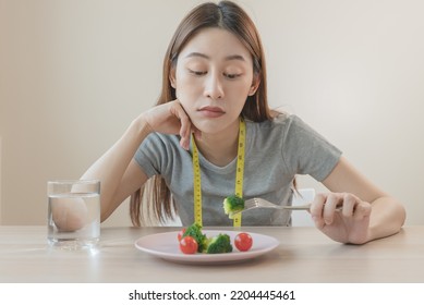 Unhappy Asian Women Is On Dieting Time Looking At Broccoli On The Fork. Girl Do Not Want To Eat Vegetables And Dislike Taste