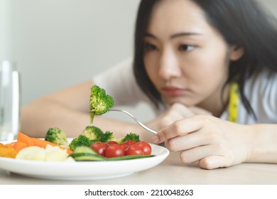 Unhappy Asian Women Is On Dieting Time Looking At Broccoli On The Fork. Girl Do Not Want To Eat Vegetables And Dislike Taste Of Broccoli.