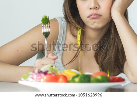 unhappy asian women is on dieting time looking at broccoli on the fork. girl do not want to eat vegetables and dislike taste of broccoli.