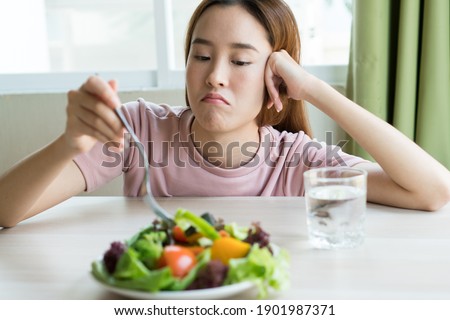 unhappy asian women is on dieting time looking at broccoli on the fork. girl do not want to eat vegetables and dislike taste of vegetable.