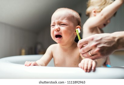 An unhappy baby girl with unrecognizable father crying when brushing teeth.