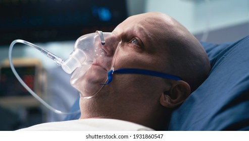 Unhappy Bald Man Breathing Oxygen From Mask Of Life Support Machine While Lying On Bed In Ward Of Oncology Clinic