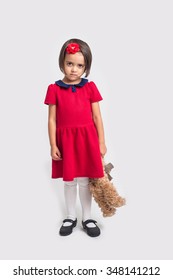 Unhappy beautiful little girl in a red dress with a toy bear