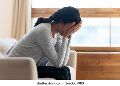 Unhappy biracial young woman sit on sofa in living room feel lonely distressed cry after breakup or divorce, upset African American millennial female suffer from depression or mental problem at home