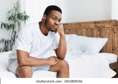 Unhappy Black Guy Sitting On Bed In Bedroom At Home. Depressed African American Man Thinking Of Life Problems. Stress, Apathy And Male Depression Concept. Free Space For Text