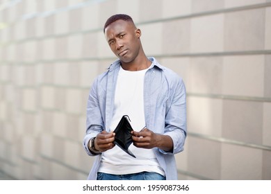 Unhappy Black Man Showing His Empty Wallet At Camera Near Brick Wall On Street. Cashless African American Guy With No Money In His Purse Outside. Financial Crisis And Poverty Concept