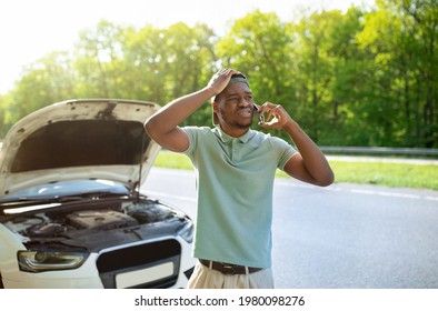 Unhappy black man standing near his broken car with open hood, experiencing engine failure, having mobile phone conversation, calling breakdown road service on smartphone - Powered by Shutterstock