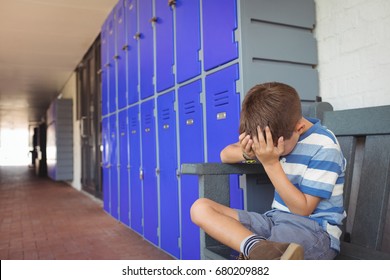 Unhappy boy sitting on bench by lockers in corridor at school - Powered by Shutterstock