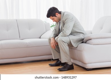 Unhappy buinessman sitting on sofa lowering his head at office