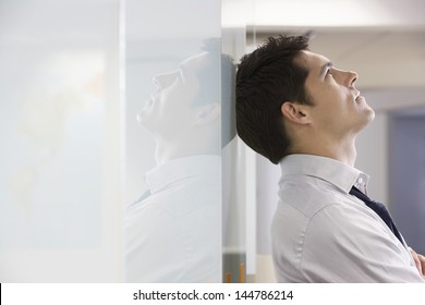 Unhappy businessman leaning back against office wall and looking at ceiling - Powered by Shutterstock